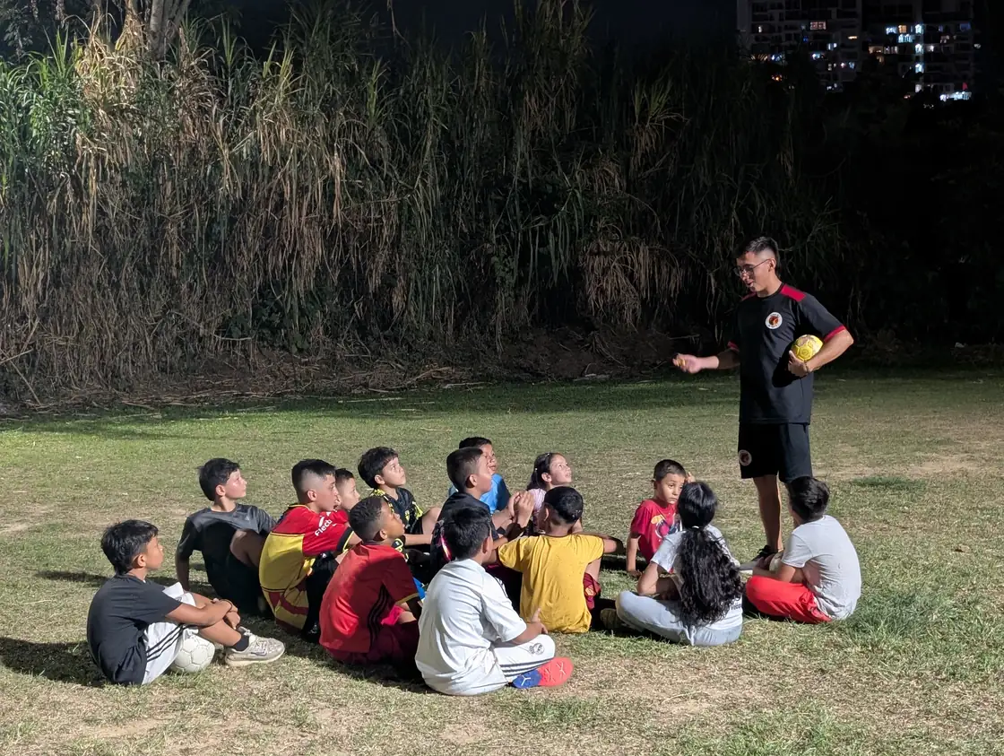 An Alpha FC coach speaking with young players seated on the field in Pereira