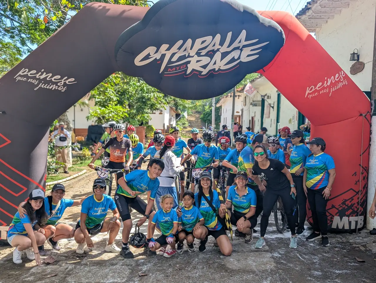 Pedalea con Conciencia participants gathered beneath a cycling event arch