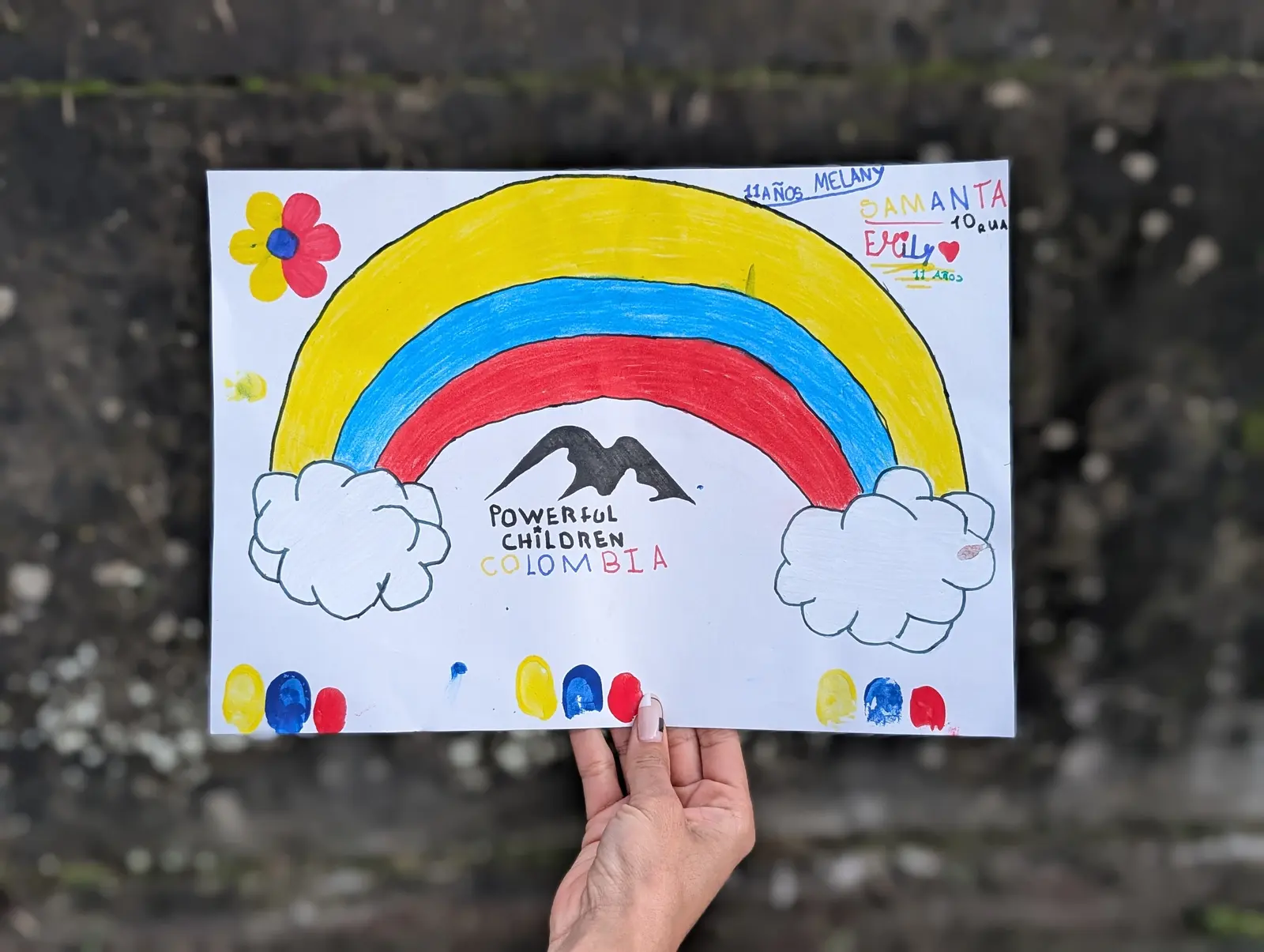 A child's drawing of the Colombian flag colors, mountains, clouds, flowers, and the Powerful Children Colombia logo